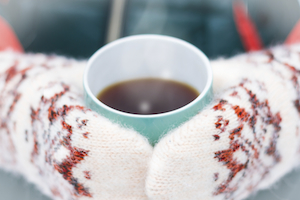 Hands in mittens holding a cup of coffee